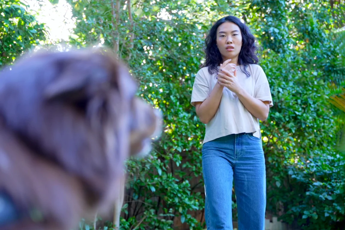 A woman on a footpath drawing back with a fearful expression as a dog approaches her