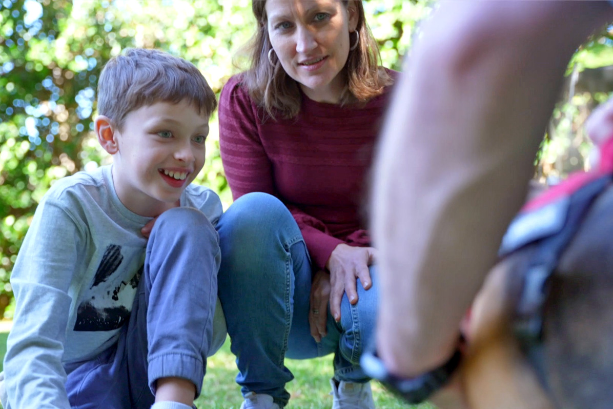 A boy crouching beside his mum as they meet a dog up close