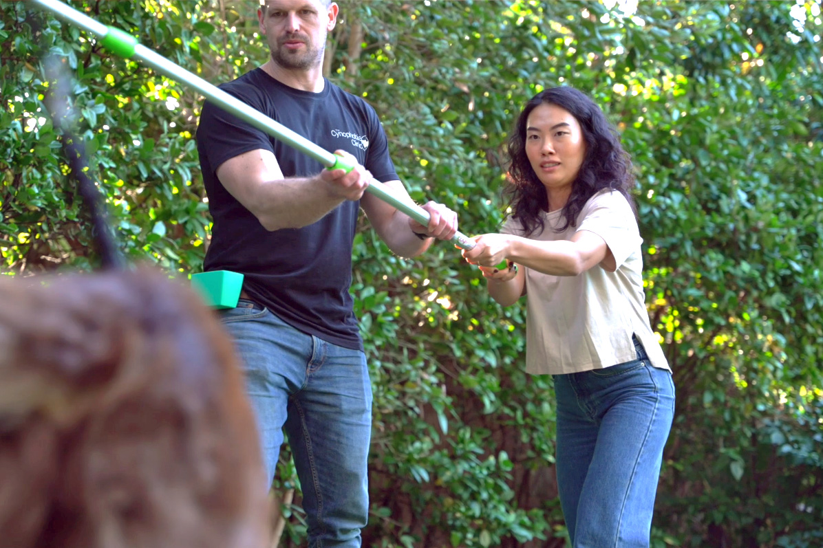 A client guiding a dog with a target stick while the clinician steadies it